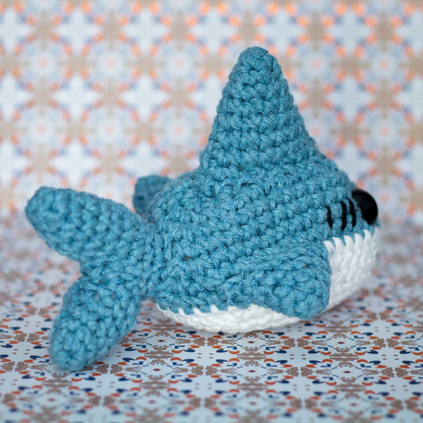 Peluche amigurumi, figurine en crochet, représentant un requin de dos, imaginé et confectionné à la main par le Rat et l'Ours.