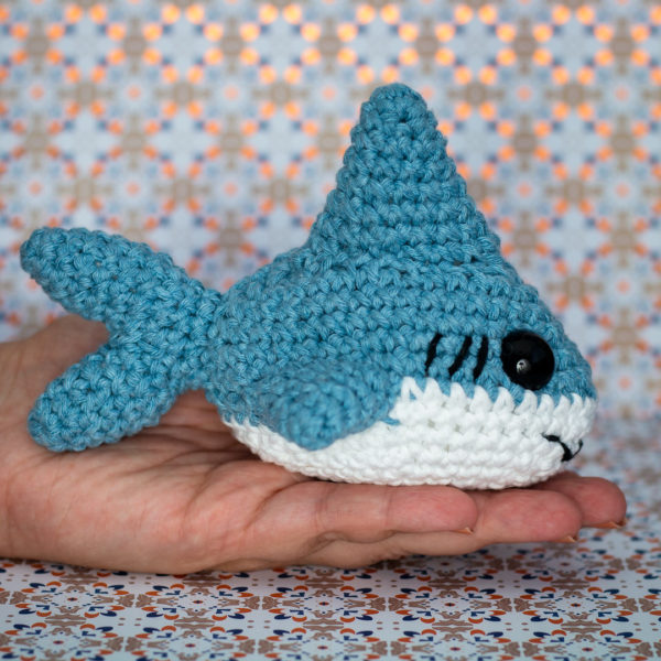 Peluche amigurumi, figurine en crochet, représentant un requin tenu en main et de profil, imaginé et confectionné à la main par le Rat et l'Ours.