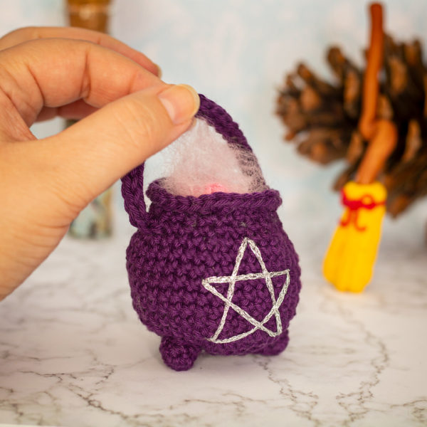Amigurumi, figurines en crochet représentant un chaudron de sorcière violet, tenu en main, imaginé et confectionné à la main par les Mignonstres, une marque le Rat et l’Ours.