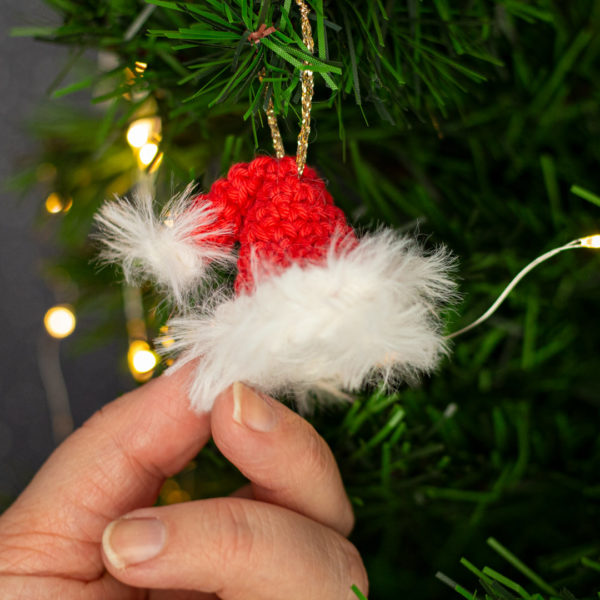 Bonnet miniature en crochet, rouge, tenu en main, imaginé et confectionné à la main par les Mignonstres, une marque le Rat et l’Ours.