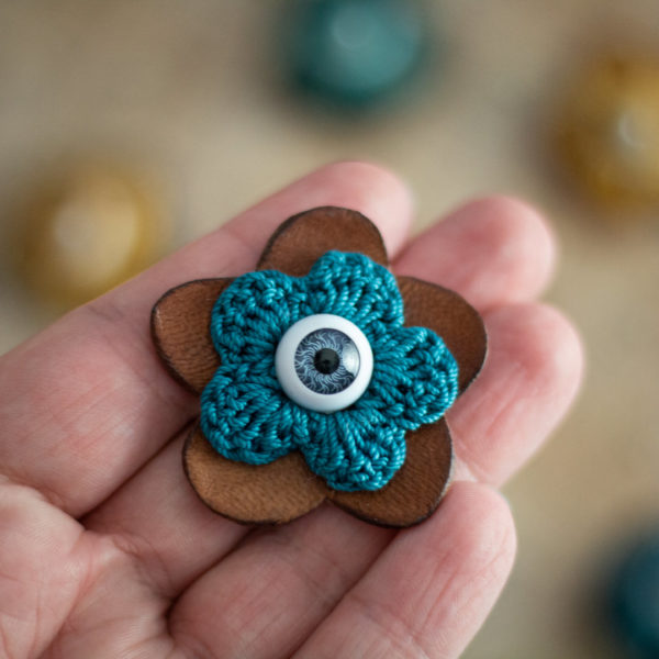 Broches en forme de fleur en cuir clair et crochet bleu (pivoine) avec un oeil au centre, imaginée et confectionnée à la main par les Mignonstres, une marque le Rat et l’Ours.