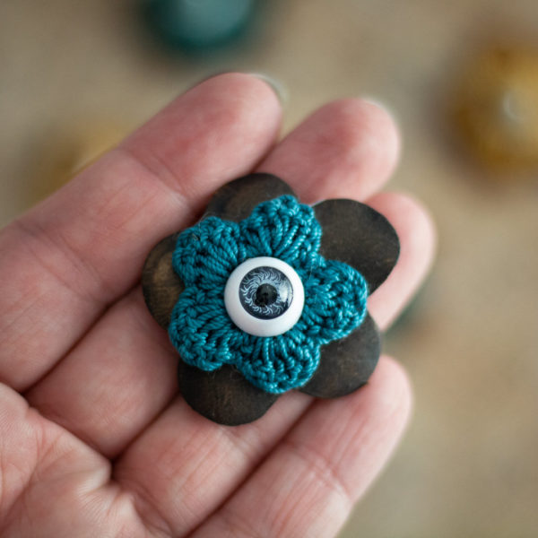 Broches en forme de fleur en cuir sombre et crochet bleu (pivoine) avec un oeil au centre, imaginée et confectionnée à la main par les Mignonstres, une marque le Rat et l’Ours.