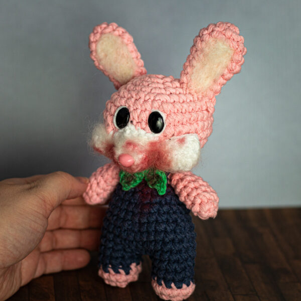 Amigurumi en crochet représentant Robbie le lapin, issu de la sage de jeu vidéo Silent Hill, tenu en main, imaginé et confectionné à la main par les Mignonstres, une marque le Rat et l’Ours.