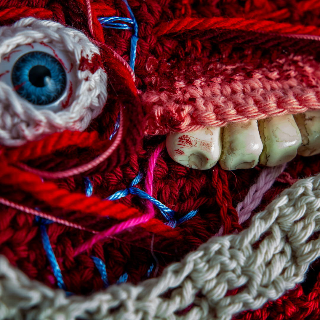 Détail d’un tableau en crochet sur le thème du body horror, avec des yeux, des dents, des instestins… Œuvre imaginée et confectionnée à la main par les Mignonstres, une marque le Rat et l’Ours.