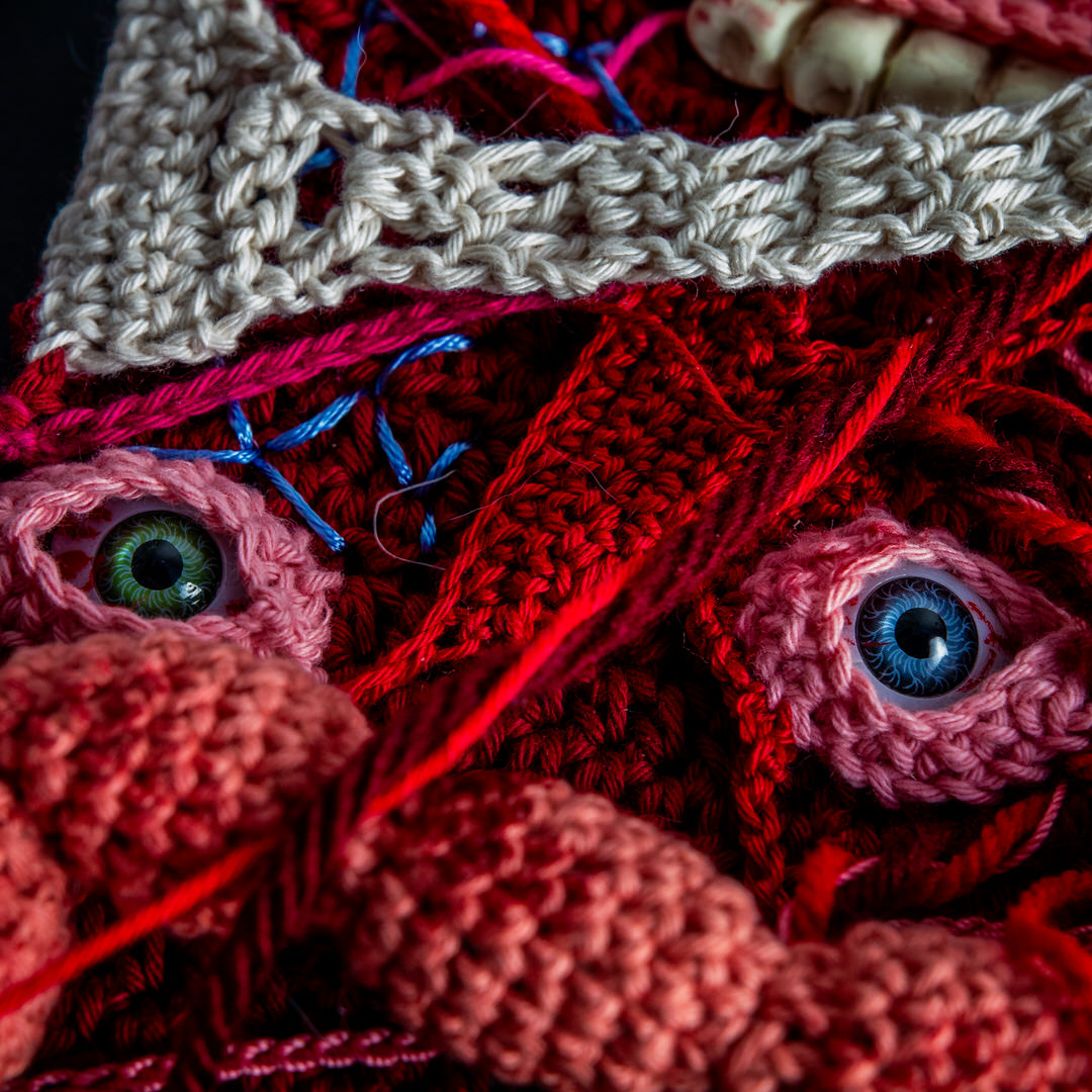 Détail d’un tableau en crochet sur le thème du body horror, avec des yeux, des dents, des instestins… Œuvre imaginée et confectionnée à la main par les Mignonstres, une marque le Rat et l’Ours.