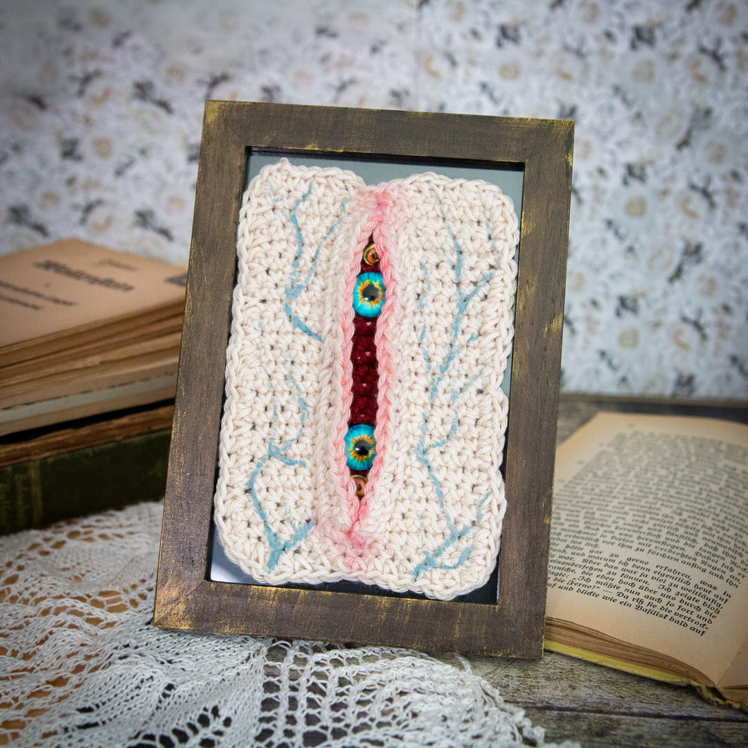 Tableau en crochet sur le thème du body horror, avec une immense blessure qui a des yeux à l'intéreiru. Œuvre imaginée et confectionnée à la main par les Mignonstres, une marque le Rat et l’Ours.